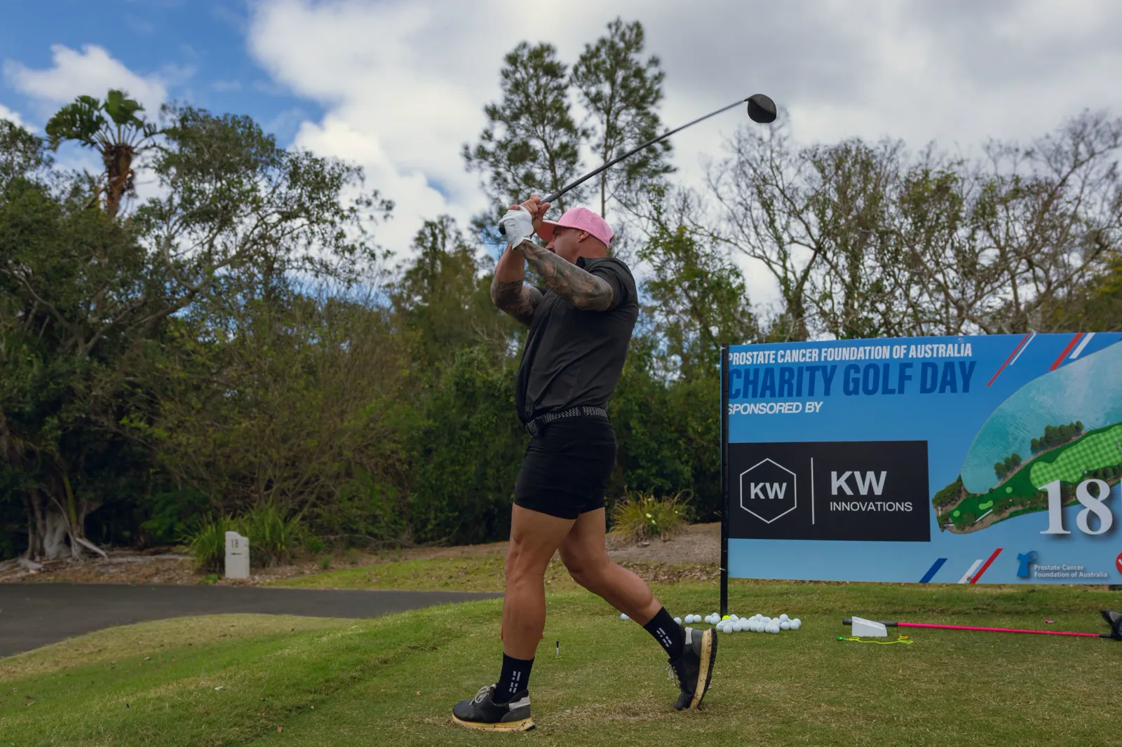 A golfer tees off on the 18th beside the Charity Golf Day sign sponsored by KW Innovations